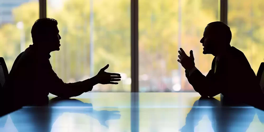 Two males sitting opposite each other about to shake hands